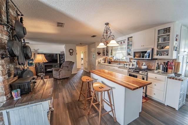 831 Plum St, Graham, TX 76450 - kitchen with appliances with stainless steel finishes, wooden counters, a kitchen breakfast bar, dark wood-style flooring, and white cabinets
