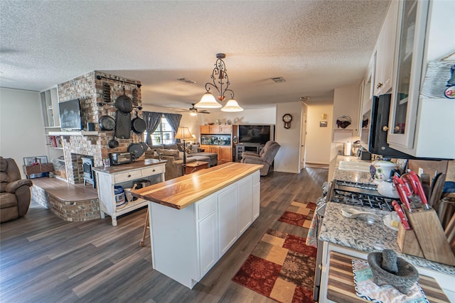 831 Plum St, Graham, TX 76450 - kitchen with butcher block countertops, open floor plan, a textured ceiling, a fireplace, and dark wood finished floors