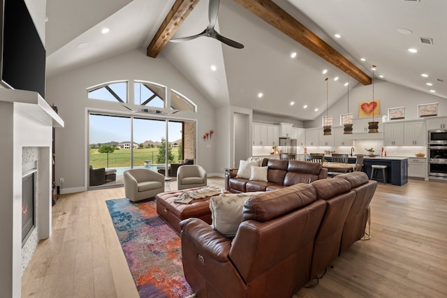 living area featuring beamed ceiling, high vaulted ceiling, ceiling fan, light wood-type flooring, and a glass covered fireplace
