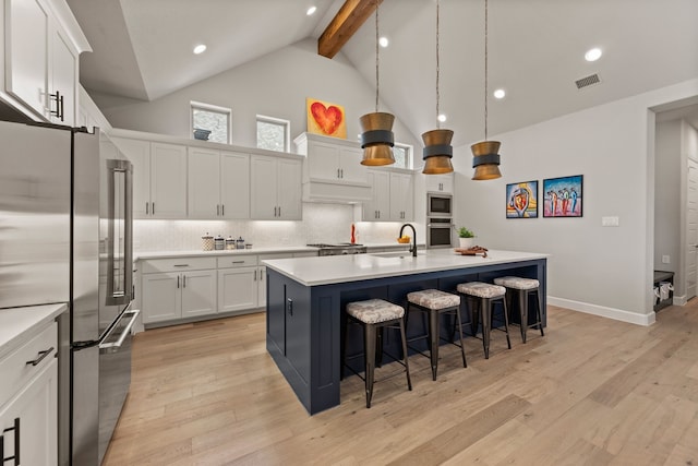 kitchen with appliances with stainless steel finishes, beam ceiling, a sink, light wood-type flooring, and high vaulted ceiling