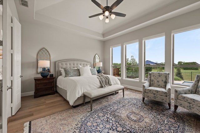 bedroom featuring light wood-type flooring, a raised ceiling, baseboards, and ceiling fan