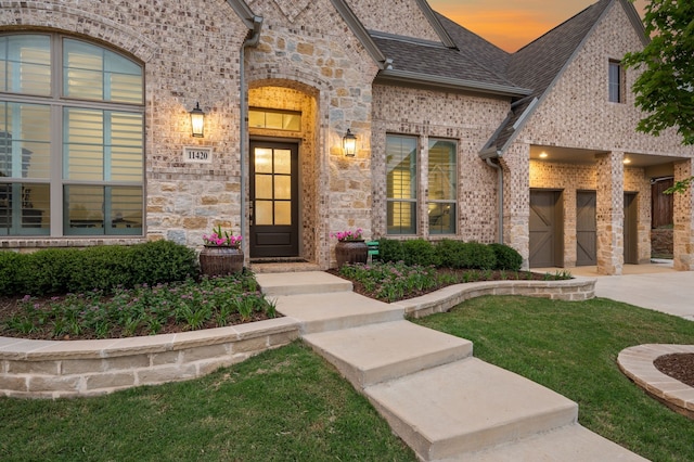 view of exterior entry featuring concrete driveway, stone siding, a yard, and brick siding