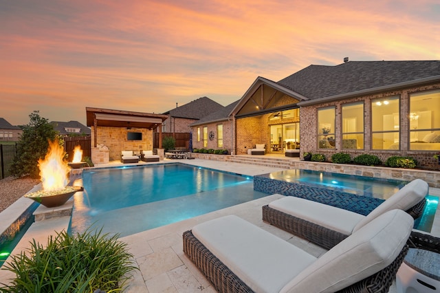pool at dusk with an in-ground hot tub, a patio, an outdoor living space with a fire pit, and fence