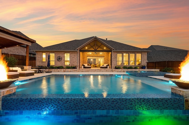 pool at dusk with an outdoor hangout area, a pool with connected hot tub, and fence