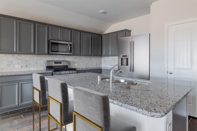 1910 Blackbird Ln, Princeton, TX 75407 - kitchen with appliances with stainless steel finishes, vaulted ceiling, decorative backsplash, light stone countertops, and a center island with sink