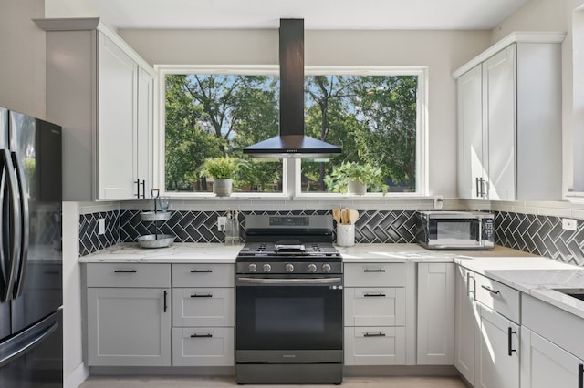 702 Griffith, Terrell, TX 75160 - kitchen featuring gas stove, freestanding refrigerator, island exhaust hood, decorative backsplash, and light stone countertops