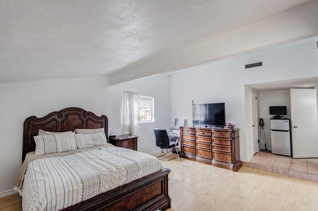 3110 Nutmeg Ln, Garland, TX 75044 - bedroom featuring freestanding refrigerator, a textured ceiling, light wood-type flooring, and baseboards