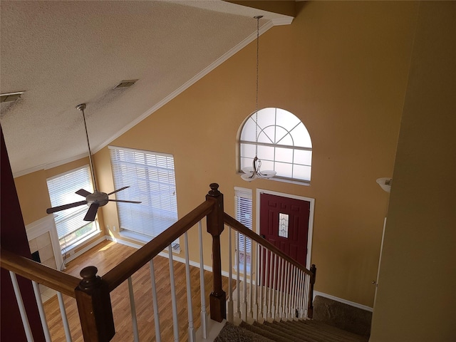 staircase featuring crown molding, a textured ceiling, a ceiling fan, a chandelier, and high vaulted ceiling