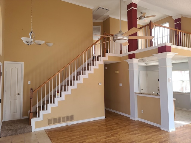 stairs with a ceiling fan, decorative columns, a high ceiling, ornamental molding, and baseboards