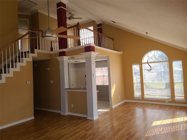 unfurnished living room with a ceiling fan, ornate columns, a textured ceiling, high vaulted ceiling, and wood finished floors