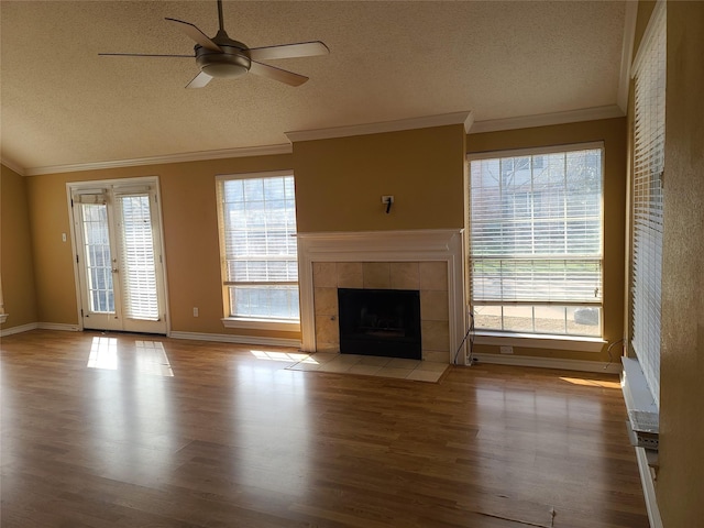 unfurnished living room featuring wood finished floors, a textured ceiling, ceiling fan, ornamental molding, and a tile fireplace