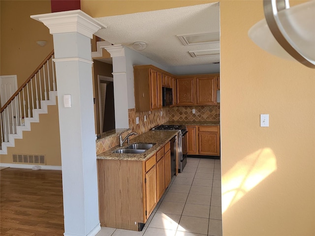 kitchen with black appliances, a sink, backsplash, stone counters, and brown cabinets