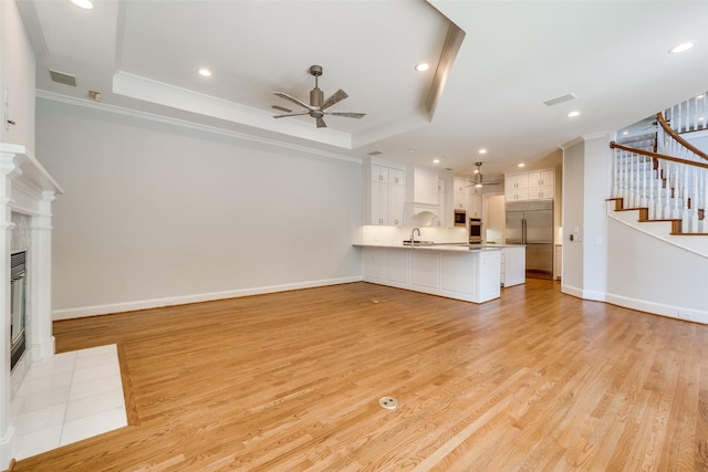 2 Birchmont Ln, Dallas, TX 75230 - unfurnished living room featuring a ceiling fan, crown molding, stairway, a tray ceiling, and light wood-type flooring