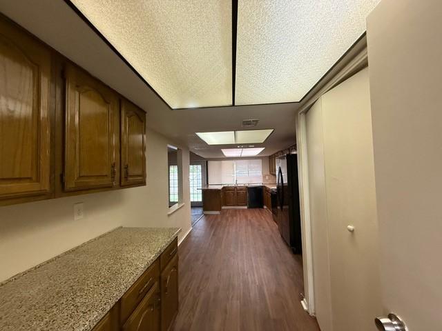 828 Wood Gln, Desoto, TX 75115 - kitchen featuring black appliances, dark wood-style flooring, light stone countertops, and brown cabinets
