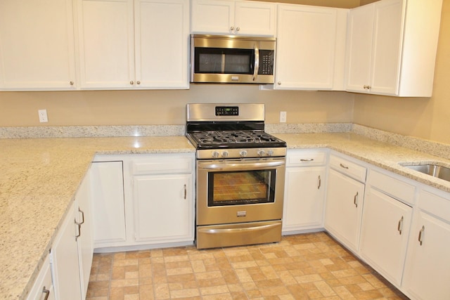 302 N 1st St, Wylie, TX 75098 - kitchen featuring appliances with stainless steel finishes, white cabinets, light stone countertops, and brick patterned flooring