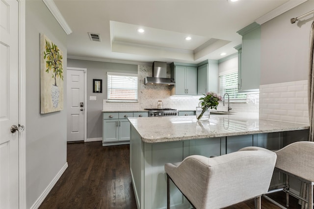 7514 Caillet St, Dallas, TX 75209 - kitchen featuring wall chimney range hood, a sink, crown molding, a tray ceiling, and dark wood-style floors