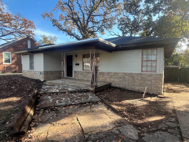 ranch-style home featuring stone siding, covered porch, and fence
