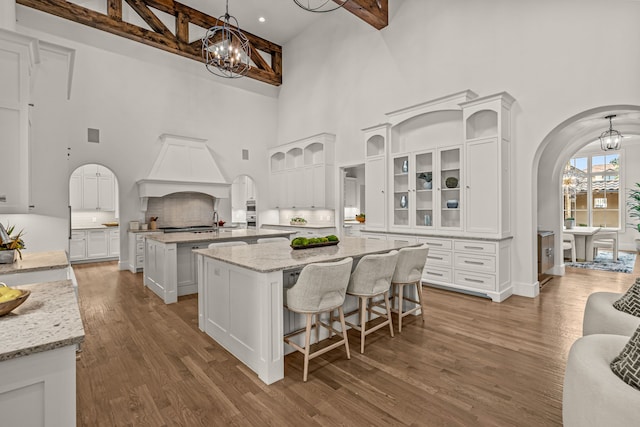 2210 Barcelona Ct, Westlake, TX 76262 - kitchen featuring a towering ceiling, an island with sink, premium range hood, arched walkways, and wood finished floors
