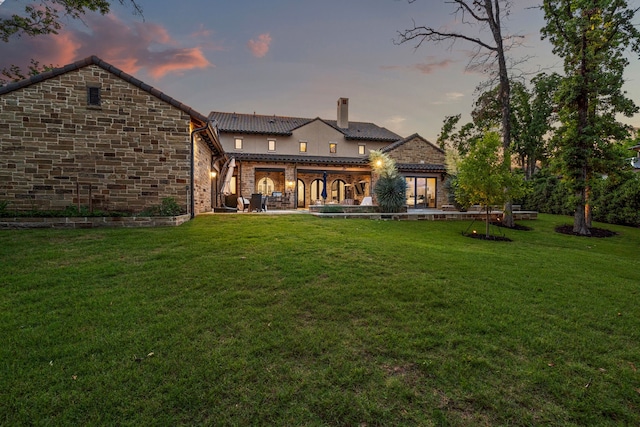 2210 Barcelona Ct, Westlake, TX 76262 - back of house at dusk with a chimney, a tiled roof, a lawn, and stone siding