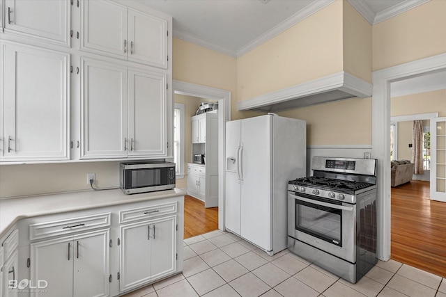 kitchen with stainless steel appliances, ornamental molding, light countertops, white cabinets, and light tile patterned flooring