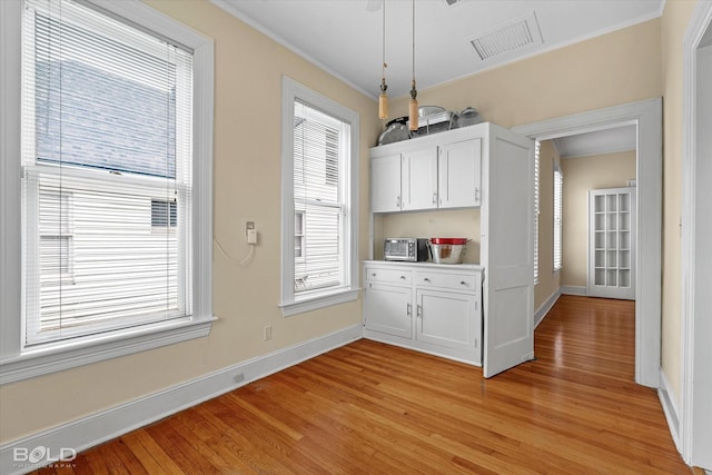 unfurnished dining area with light wood-style floors, crown molding, and baseboards