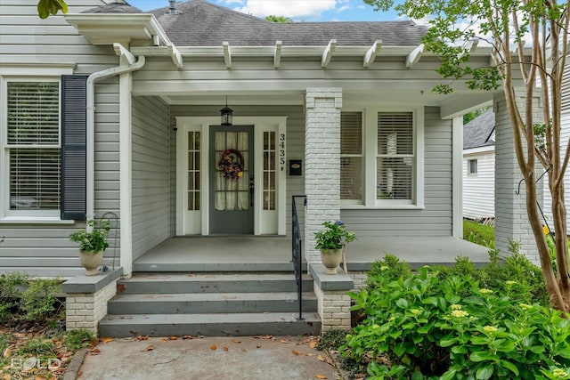 doorway to property with roof with shingles and a porch