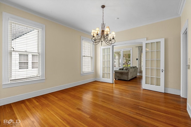 spare room featuring french doors, light wood-type flooring, baseboards, crown molding, and a chandelier