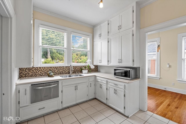 kitchen featuring stainless steel microwave, a sink, decorative backsplash, light countertops, and white cabinets