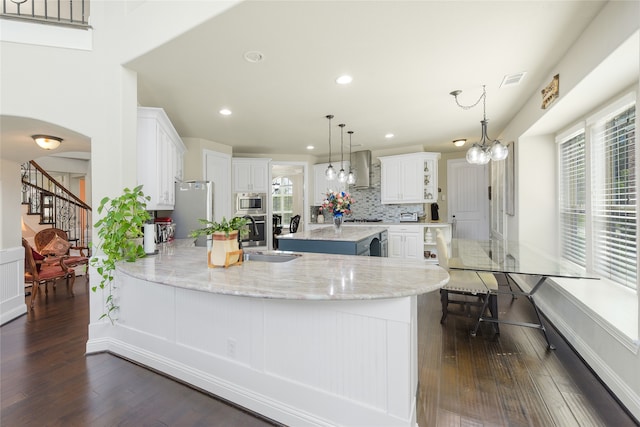 215 Dominion Dr, Wylie, TX 75098 - kitchen featuring wall chimney range hood, a sink, stainless steel appliances, a peninsula, and dark wood-style floors