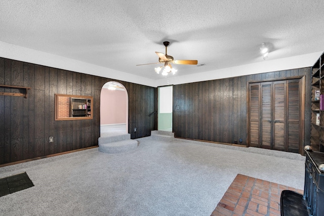 510 Allen Ave, Duncanville, TX 75137 - unfurnished living room featuring wooden walls, ceiling fan, arched walkways, a textured ceiling, and carpet