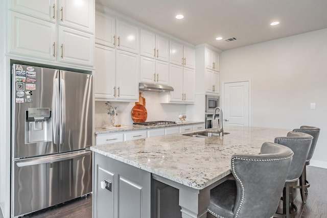 3723 Birch Wood Ct, Northlake, TX 76226 - kitchen with appliances with stainless steel finishes, under cabinet range hood, dark wood-style flooring, white cabinets, and an island with sink