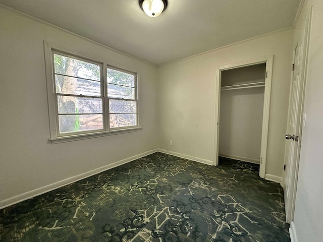 unfurnished bedroom featuring ornamental molding, dark colored carpet, baseboards, and a closet