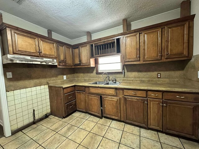 kitchen featuring a sink, under cabinet range hood, light tile patterned flooring, a textured ceiling, and ornamental molding