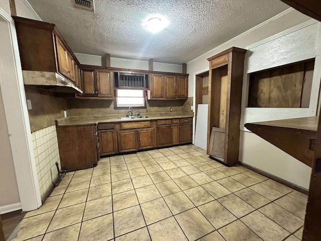 kitchen with a sink, a textured ceiling, light tile patterned flooring, and crown molding