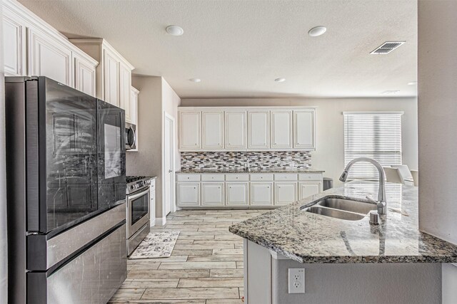 3001 Spring Ct, Midlothian, TX 76065 - kitchen featuring stainless steel appliances, a sink, light wood finished floors, light stone countertops, and white cabinets
