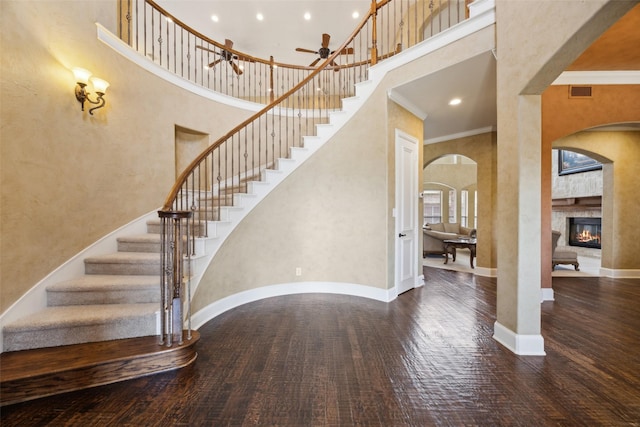 1270 Timber Ln, Frisco, TX 75036 - staircase with a towering ceiling, arched walkways, a stone fireplace, wood finished floors, and ceiling fan