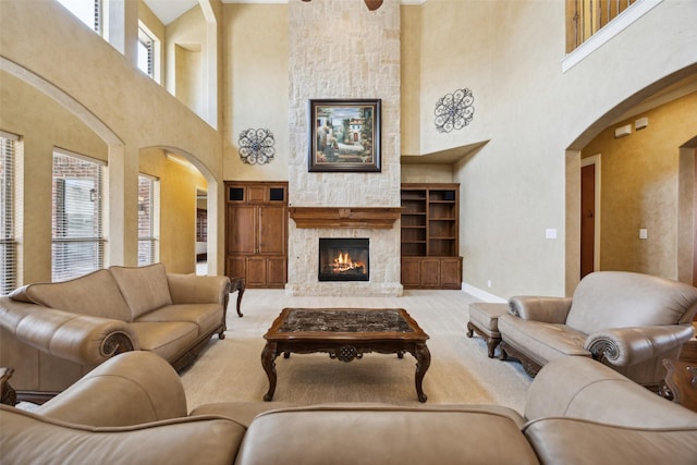 1270 Timber Ln, Frisco, TX 75036 - carpeted living area featuring a towering ceiling, arched walkways, a stone fireplace, baseboards, and a ceiling fan