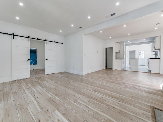 809 Cristler Ave, Dallas, TX 75223 - unfurnished living room with a barn door, light wood-style floors, baseboards, and recessed lighting
