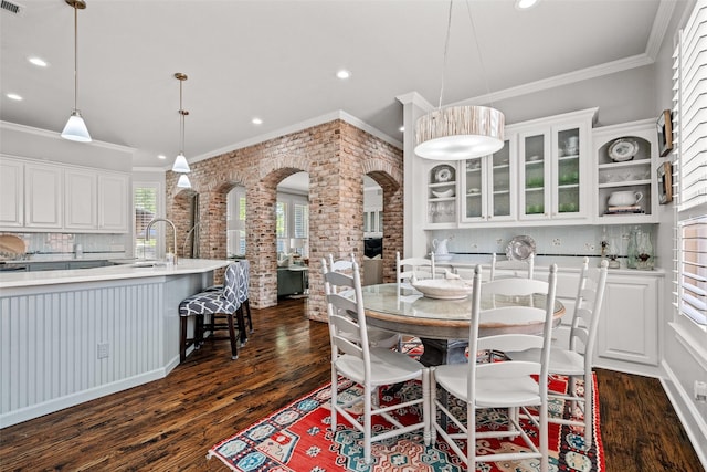 903 Crescent Dr, Highland Village, TX 75077 - dining room featuring recessed lighting, dark wood-type flooring, ornamental molding, arched walkways, and brick wall