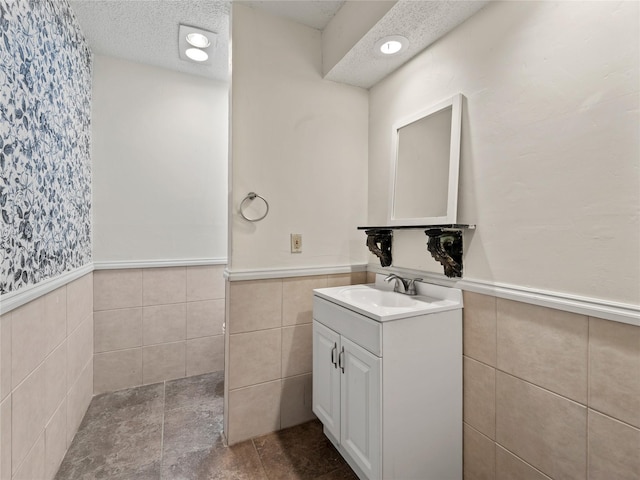 12605 Burninglog Ln, Dallas, TX 75243 - bathroom with a wainscoted wall, tile walls, vanity, and a textured ceiling