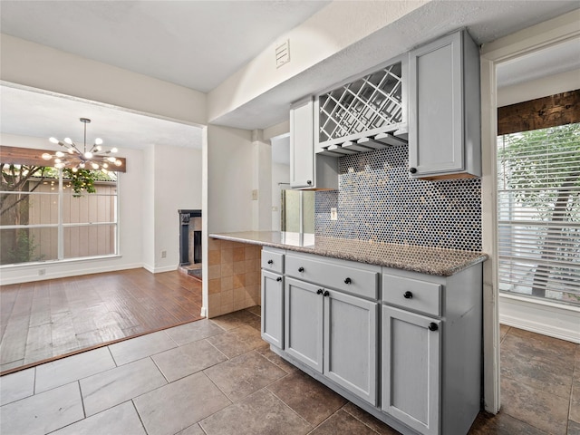 12605 Burninglog Ln, Dallas, TX 75243 - kitchen featuring gray cabinetry, decorative backsplash, a chandelier, baseboards, and light stone counters