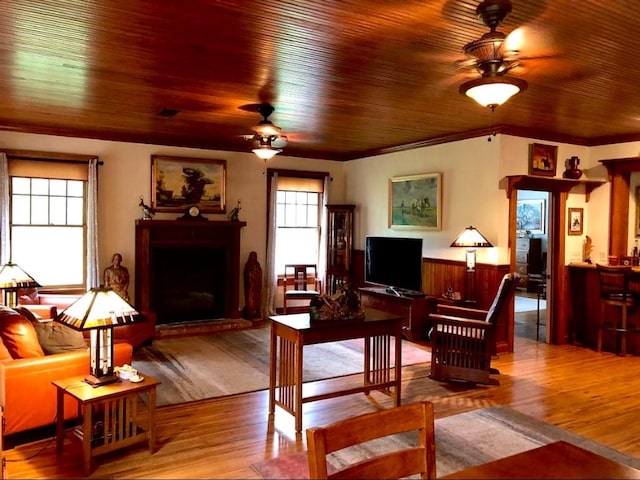 1001 S Locust St, Clarksville, TX 75426 - living room featuring ceiling fan, a fireplace with raised hearth, wood finished floors, wood ceiling, and a wainscoted wall