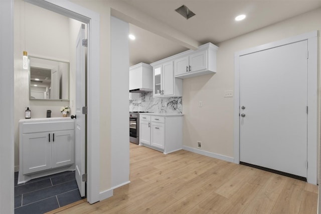 1832 Arch St, Fort Worth, TX 76105 - kitchen with stainless steel stove, decorative backsplash, white cabinetry, light wood finished floors, and light countertops