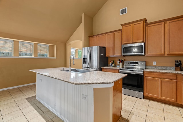632 Shotwell St, Crowley, TX 76036 - kitchen with appliances with stainless steel finishes, light tile patterned flooring, high vaulted ceiling, a kitchen island with sink, and brown cabinetry