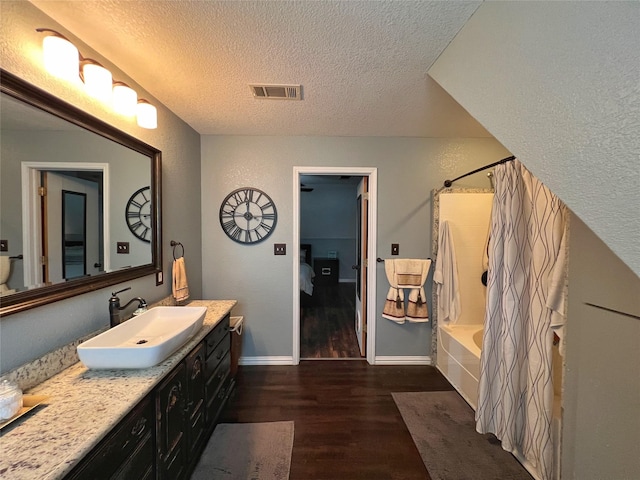 full bathroom with a textured ceiling, wood finished floors, shower / bathtub combination with curtain, vanity, and baseboards