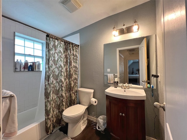 bathroom featuring toilet, vanity, a textured wall, shower / bathtub combination with curtain, and wood finished floors