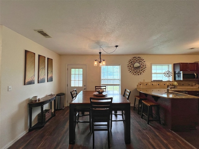 dining room with dark wood finished floors, a chandelier, a textured ceiling, and baseboards