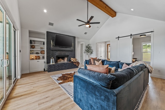 5219 Old Dennis Rd, Weatherford, TX 76087 - living area with ceiling fan, a barn door, beam ceiling, light wood-style floors, and a brick fireplace