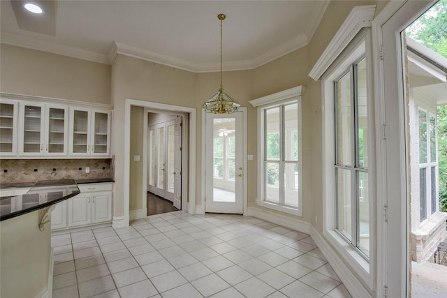 7712 Ravenswood Rd, Granbury, TX 76049 - kitchen featuring a chandelier, glass insert cabinets, dark countertops, healthy amount of natural light, and ornamental molding