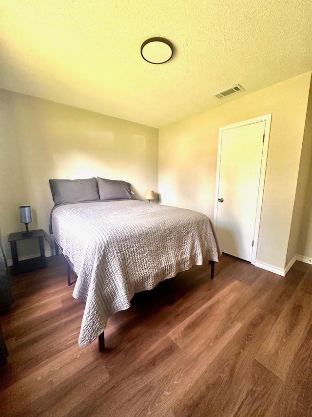 bedroom with wood finished floors, baseboards, and a textured ceiling